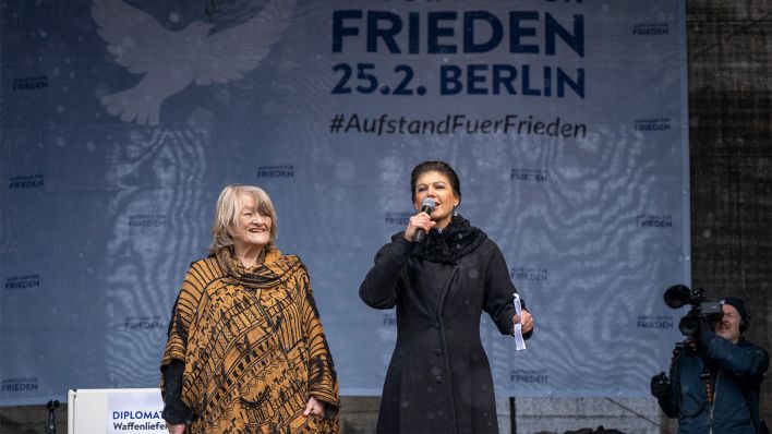 Alice Schwarzer (l) und Sahra Wagenknecht (r) stehen während einer Demonstration auf einer Bühne (Bild: dpa/Monika Skolimowska)