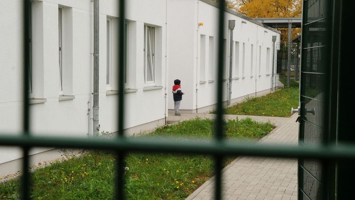 Symbolbild:Ein kleiner Junge steht an einer Aufnahmeeinrichtung für Asylbewerbende.(Quelle:dpa/B.Settnik)