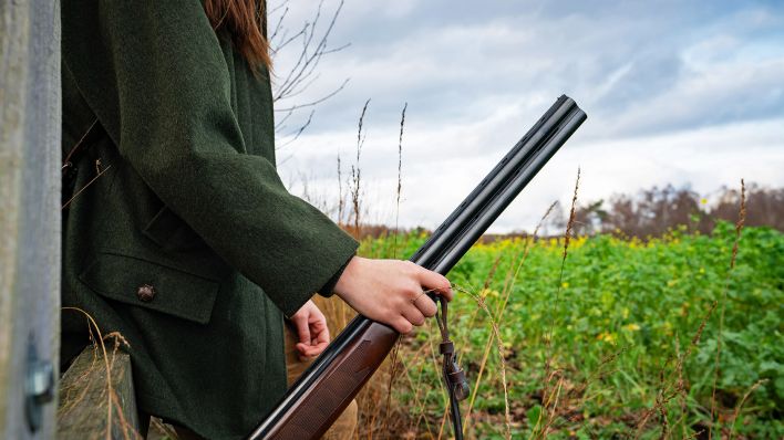 Eine Jägerin mit einem Gewehr in der Hand vor einem Feld.(Quelle:dpa/Countrypixel)