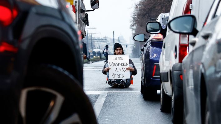 Ein Aktivist zeigt ein Schild mit der Aufschrift „Lieber Wegsperren als Reden“ bei einer Sitzblockade mit weiteren Aktivisten auf der Prenzlauer Allee (Bild: dpa/Carsten Koall)