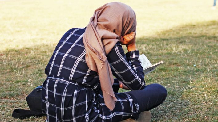 Symbolbild:Eine Muslima mit Kopftuch sitzt auf einer Wiese und liest ein Buch.(Quelle:dpa/W.Steinberg)
