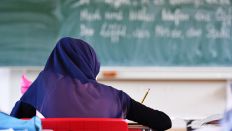 Symbolbild:Eine Frau mit einem Kopftuch schreibt etwas in einem Klassenzimmer auf.(Quelle:dpa/U.Anspach)