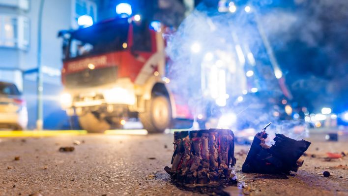 Symbolbild: Ausgebranntes Silvester-Feuerwerk vor einem Feuerwehrfahrzeug. (Quelle: imago images/M. Schwarz)