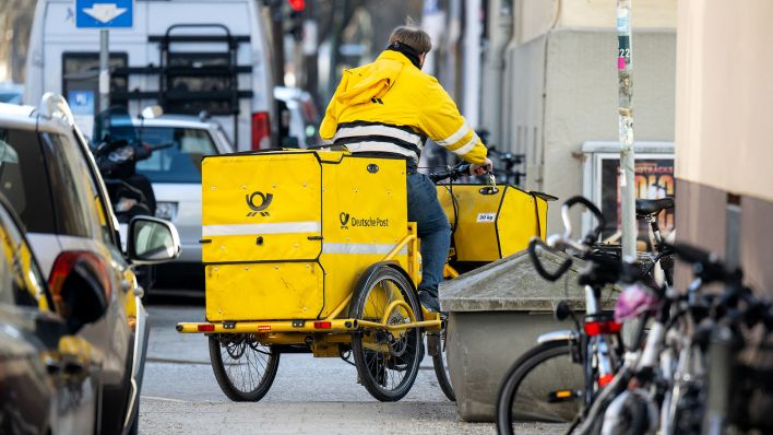 Ein Briefträger fährt mit seinem Fahrrad eine Straße entlang. (Quelle: dpa/Sven Hoppe)