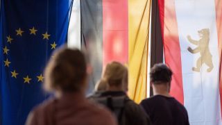 Archivbild: Wähler stehen in einem Wahllokal vor einer Europa-, Deutschland- und Berlinflagge (l-r). (Quelle: dpa/S. Gollnow)