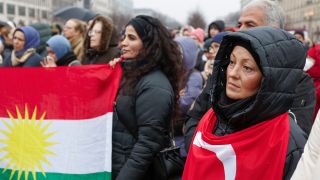 Trauernde haben sich zu einer Gedenkveranstaltung fuer die Opfer des Erdbebens in der Tuerkei und Syrien am Brandenburger Tor versammelt und ziegen eine kurdische und eine tuerkische Flagge. (Quelle: Imago Images/Jochen Eckel)