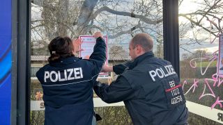 Zwei Polizeibeamte kleben Fahndungsplakate in einer Bushaltestelle in Nauen an. Die Polizei sucht nach einem aus der Sicherungsverwahrung entflohenen Sexualstrafttäter. (Quelle: rbb/Juliane Gunser)