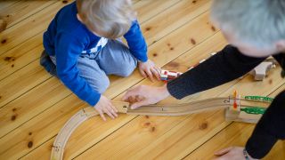 Symbolfoto: Ein Kleinkind und eine Frau spielen auf dem Fussboden mit einer Holzeisenbahn. (Quelle: dpa/T.Trutschel)