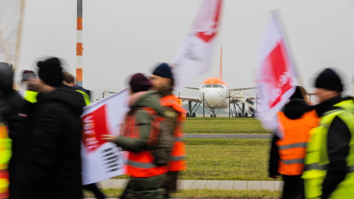 Teilnehmer einer Demonstration zum Warnstreik am Flughafen Berlin-Brandenburg BER gehen am 25.01.2023 an einem geparkten Flugzeug vorbei. (Quelle: dpa/Christoph Soeder)