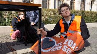 Klimaaktivist Henning Jeschke (r) von der Letzten Generation sitzt am 23.03.2023 bei einer Protestaktion vor dem Bundesverkehrsministerium.