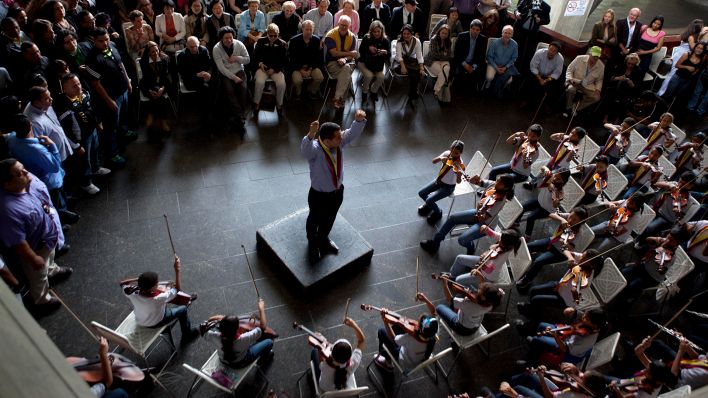 Symbolbild: Ein Mann dirigiert vor Publikum den Auftritt eines Jugendorchesters