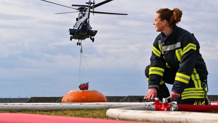 Ronja Marschler von der Freiwilligen Feuerwehr Eggersdorf beobachtet einen Hubschrauber vom Typ AS 332 Super Puma der Bundespolizei, der Wasser aus einem mobilen Tank während einer Übung am 30.03.2023 holt.(Quelle:dpa/P.Pleul)