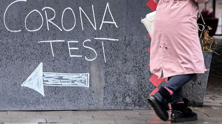 "Kostenlos Coronatest" steht auf einer Tafel und weist den Weg zu einer Teststation. (Quelle: dpa/Jens Kalaene)