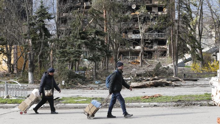 Archivbild: Zwei Personen gehen eine Straße in der Nähe eines beschädigten Gebäudes in Mariupol entlang. (Quelle: dpa/XinHua)