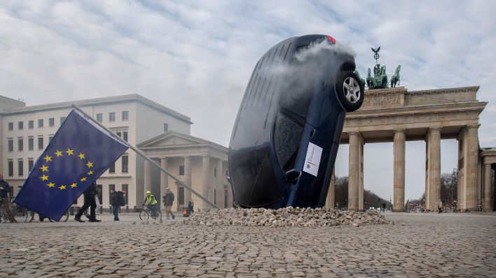 Ein SUV steckt scheinbar im Boden vor dem Brandenburger Tor, aus dem Heckbereich steigt Qualm. Mit dieser Aktion protestieren Umweltschutz-Aktivisten von Greenpeace gegen die Verkehrspolitik der Bundesregierung. (Quelle: dpa/P. Zinken)
