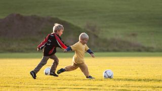 Kinder spielen auf einer Wiese Fußball (Quelle: IMAGO/JOKER)