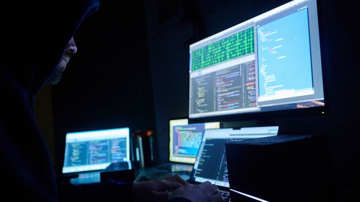Symbolbild: Fiktive html-Seiten und Hacker-Programme sind auf Bildschirmen zu sehen, während ein Mann seinen Hände auf der Tastatur hat. (Quelle: dpa/Annette Riedl)