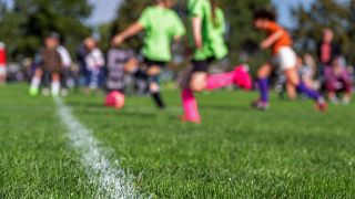 Symbolbild:Kinder spielen in bunten Trikots Fussball auf einem Rasenfeld.(Quelle:dpa/S.White)