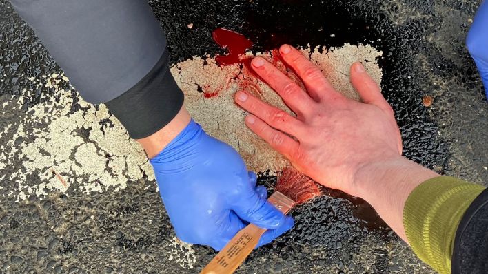 Die Hand eines Klima-Aktivisten wird vom Asphalt einer Straße mit Öl gelöst (Quelle: DPA/Ann-Marie Utz)