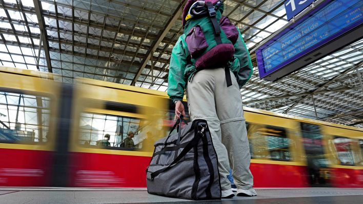 Symbolbild:Eine Reisende mit Gepäck steht am Gleis, während eine S-Bahn an ihr vorbeifährt.(Quelle:dpa/M.Sohn)