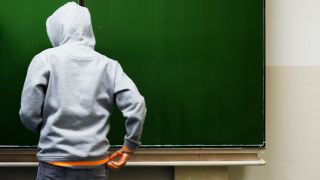 Symbolbild:Ein Schüler in einem Kapuzenpullover steht vor einer Tafel.(Quelle:dpa/J.Stratenschulte)