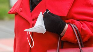 Frau im roten Mantel häkt FFP2-Maske in der Hand (Bild: imago images/Michael Gstettenbauer)