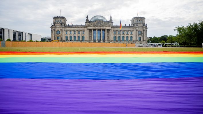 Eine riesige Regenbogenfahne liegt am 23.05.2023 bei einer Aktion der Initiative "Grundgesetz für Alle" für die Rechte und den verfassungsmäßigen Schutz der Rechte queerer Menschen vor dem Reichstagsgebäude. (Quelle: Picture Alliance/dpa/Christoph Soeder)