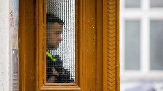 Ein Polizist steht am 24.05.2023 bei einer Hausdurchsuchung in Berlin-Kreuzberg in einem Gebäudeeingang. (Quelle: dpa/Christoph Soeder)