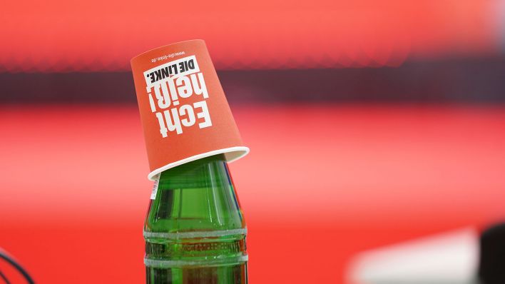 Ein Becher mit dem Logo der Partei Die Linke steht kopfüber auf einer Wasserflasche (Quelle: Flashpic/Jens Krick)