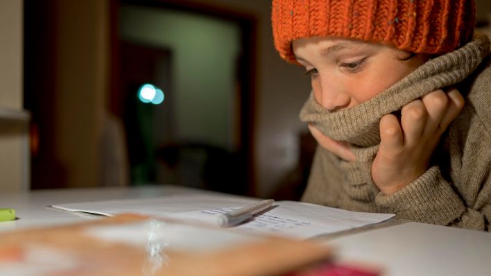 Symbolbild:Ein Kind in Winterkleidung sitzt an seinen Hausaufgaben an einem Tisch.(Quelle:dpa/A.Amraeva)