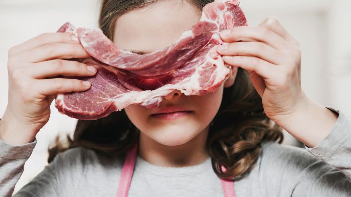 Symbolbild: Ein junges Mädchen hält sich ein Stück rohes Fleisch vors Gesicht. (Quelle: dpa/F. Kopola)