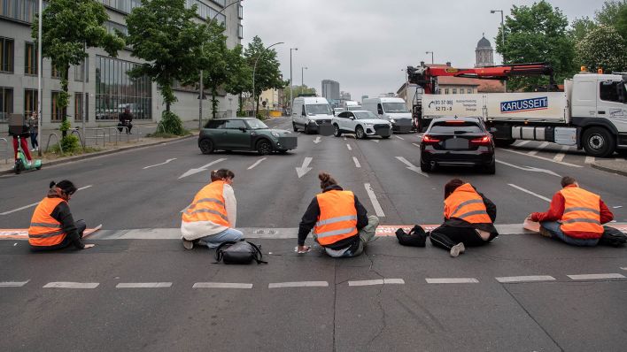 Symbolbild: Bei einer Straßenblockade der Letzten Generation sitzen Aktivisten auf dem Mühlendamm auf der Straße. (Quelle: dpa/P. Zinken)
