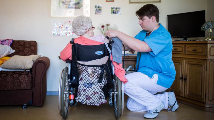 Symbolbild: Eine maennliche Pflegekraft misst Blutdruck bei einer aelteren Frau im Rollstuhl. (Quelle: dpa/F. Gaertner)