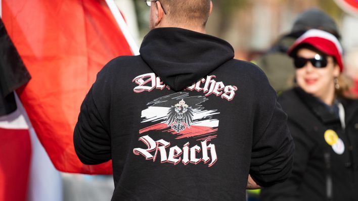 Symbolbild: Ein Mann trägt einen Pullover mit dem Aufdruck „"Deutsches Reich" bei einer Demonstration von Reichsbürgern. (Quelle: dpa/C. Gateau)