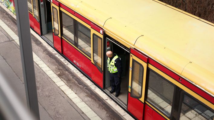 Eine S-Bahn der Linie S1 steht im Bezirk Steglitz-Zehlendorf an der S-Bahnstation Sundgauer Straße und ein Sicherheitsmitarbeitder der Bahn schaut durch eine Tür nach Draußen. (Quelle: Wolfram Steinberg/dpa)