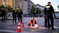 Eine Aktivistin, die sich am 19.05.2023 auf einer Berliner Straß festgeklebt hat, ist von Einsatzkräften der Polizei umringt.(Quelle:AP/M.Schreiber)