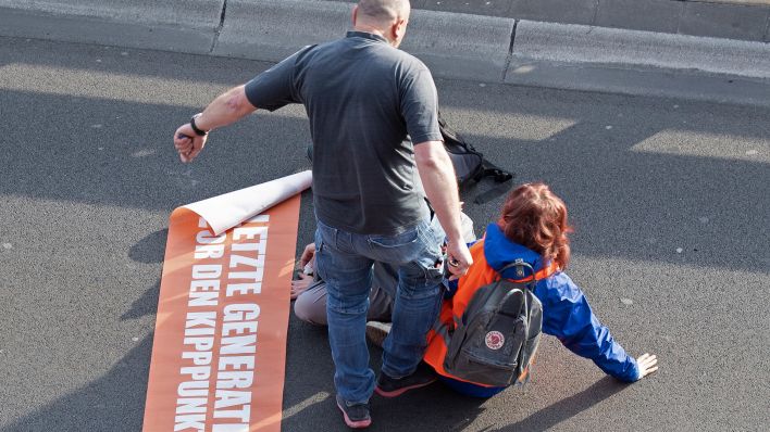 Bei einer Blockade der Gruppe Letzte Generation auf der Stadtautobahn unweit des Kurfürstendamms tritt ein Mann am 19.05.2023 gegen einen Aktivisten (Quelle: dpa/Paul Zinken)