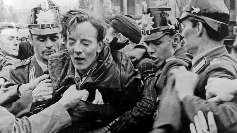 Archivbild:17.06.1953:Ein kommunistischer Agitator, der von der demonstrierenden Menschenmenge zusammengeschlagen wurde, wird an der Sektorengrenze von Westberliner Polizisten geschützt. (Quelle:UPI)