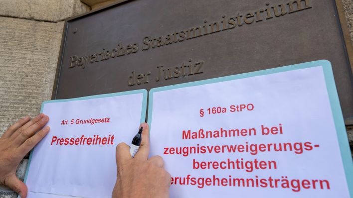 Gesetzestexte werden von einer Person bei einer Protestaktion am Eingang des Justizministerium in München angebracht. (Quelle: dpa/Peter Kneffel)