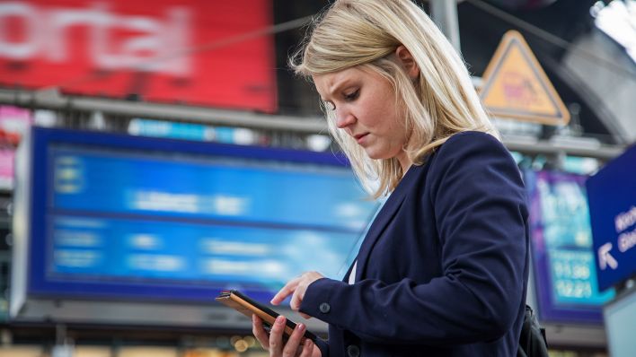 Symbolbild:Eine Frau steht am Bahnhof und schaut auf ihr Handy.(Quelle:dpa/C.Klose)