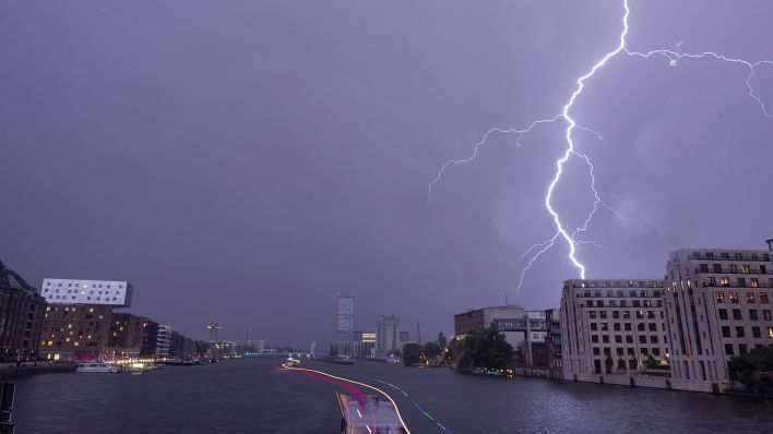 Ein Blitz entlädt sich am späten Abend über der Spree in Richtung Elsenbrücke am Himmel (Bild: dpa/Paul Zinken)