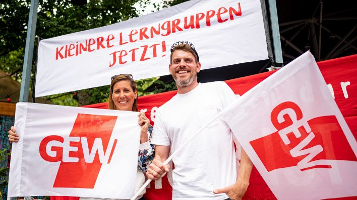 Sven und Bianca, beide Lehrer an einer Neuköllner Schule, stehen am 06.06.2023 mit zwei GEW-Flaggen beim Warnstreiks an den Berliner Schulen in Berlin-Kreuzberg vor einem Banner mit der Aufschrift „Kleinere Lerngruppen jetzt!“.(Quelle:dpa/F.Sommer)