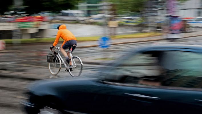Symbolbild:Ein PKW fährt hinter einem Fahrradfahrer an einer Kreuzung einer Hauptverkehrsstrasse.(Quelle:dpa/C.Koall)