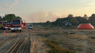 Feuerwehrkräfte sind neben einem Löschhubschrauber in einem Waldstück nahe Jüterbog im Einsatz. (Quelle: dpa/Sven Kaeuler)