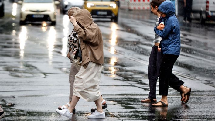 Symbolbild: Vier Frauen versuchen sich beim ueberqueren einer Strasse vor dem Regen zu schuetzen. (Quelle: dpa/J. Eckel)