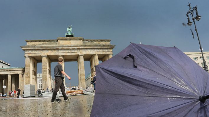 Symbolbild: Ein liegengelassener Regenschirm ist vor dem Brandenburger Tor in Berlin nach einem Regenschauer zu sehen. (Quelle: dpa/S. Pilick)