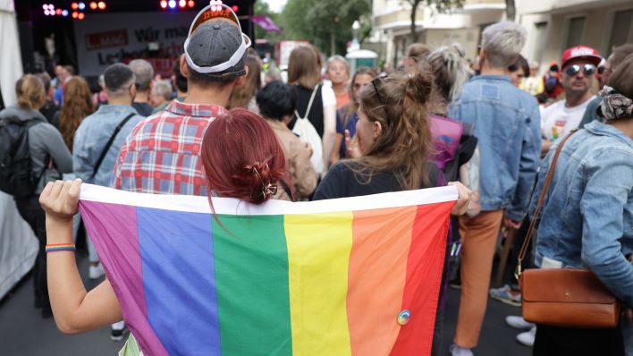 Archivbild: Eine Besucherin des 28. Lesbisch-Schwulen Stadtfestes rund um den Nollendorfplatz trägt im Juli 2022 vor einer Bühne eine Regenbogenfahne. (Quelle: dpa/Jörg Carstensen)