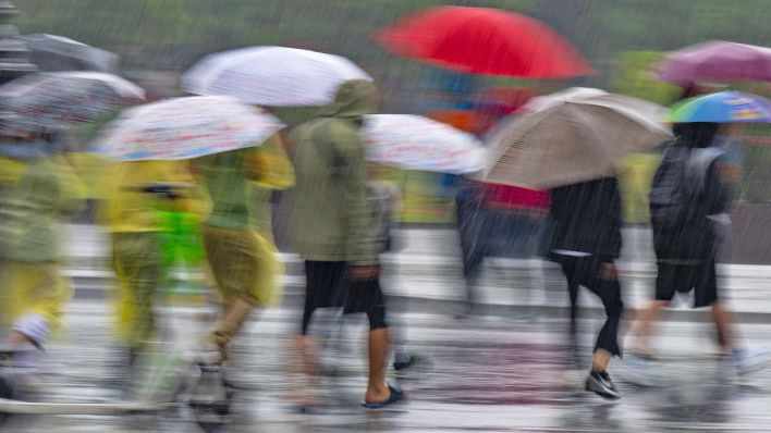 Touristen mit Regenschirmen und Regenponchos gehen am 23.06.2023 bei strömenden Regen über die Straße Unter den Linden. (Quelle: dpa/Monika Skolimowska)