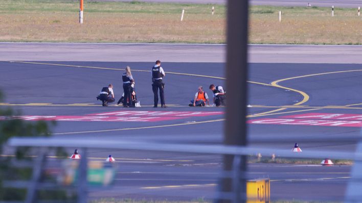 Polizisten stehen am 13.07.2023 auf dem Flugfeld und versuchen Aktivisten der Gruppe Letzte Generation am Flughafen vom Asphalt zu lösen (Quelle: dpa/David Young)