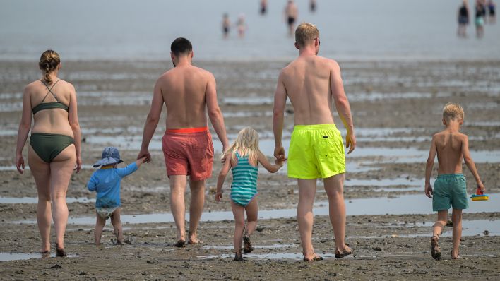 Mehrere Personen gehen mit Kindern an einem Strand in Richtung Meer